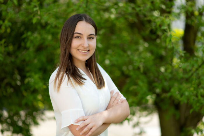 Bewerbungsfoto draussen im Gründen von einer jungen Frau in weisser Bluse