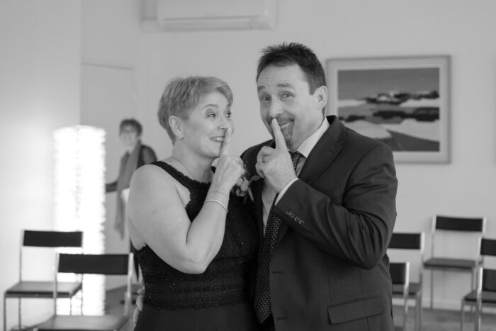 Zivilhochzeit. Brautpaar hält sich den Zeigefinger vor den Mund (Stillschweigen)