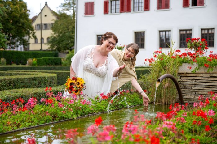 Braut mit Trauzeugin bei Brunnen stehend